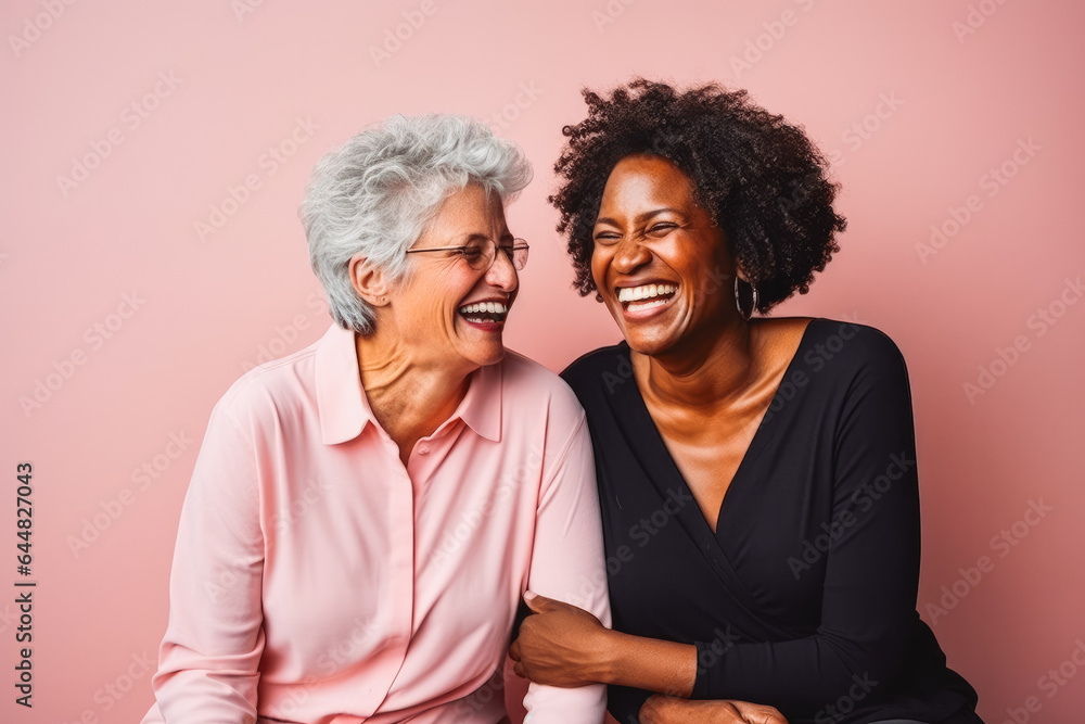 Portrait of two older female interracial best friends laughing, smiling and hugging on solid studio background. Portrait of two older female interracial best friends laughing, smiling and hugging on solid studio background.