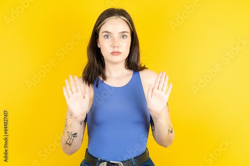 Serious Beautiful woman wearing blue tank top pulls palms towards camera, makes stop gesture, asks to control your emotions and not be nervous photo