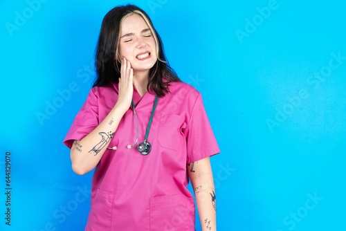 Foto Young caucasian doctor woman wearing pink medical uniform touching mouth with hand with painful expression because of toothache or dental illness on teeth