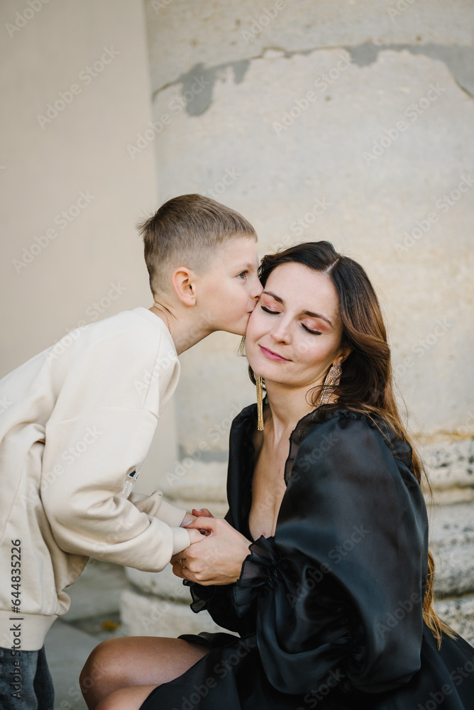 Mother hold hands son stands on stairs near large columns of ancient temple at sunset. Parent kiss kid boy walk on autumn day. Child hugs mom near Baroque Catholic church in Pidhirtsi Lviv Ukraine Mother hold hands son stands on stairs near large columns of ancient temple at sunset. Parent kiss kid boy walk on autumn day. Child hugs mom near Baroque Catholic church in Pidhirtsi Lviv Ukraine