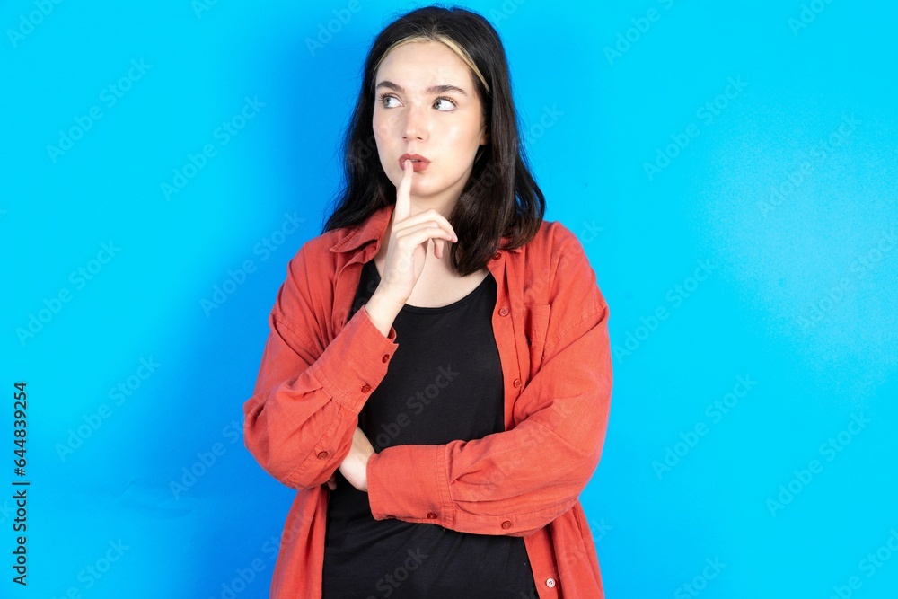 Beautiful woman wearing red jacket silence gesture keeps index finger to lips makes hush sign. Asks not to share secret Beautiful woman wearing red jacket silence gesture keeps index finger to lips makes hush sign. Asks not to share secret