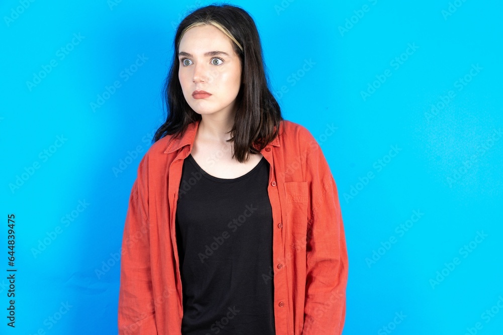 Beautiful woman wearing red jacket stares aside with wondered expression has speechless expression. Embarrassed model looks in surprise Beautiful woman wearing red jacket stares aside with wondered expression has speechless expression. Embarrassed model looks in surprise