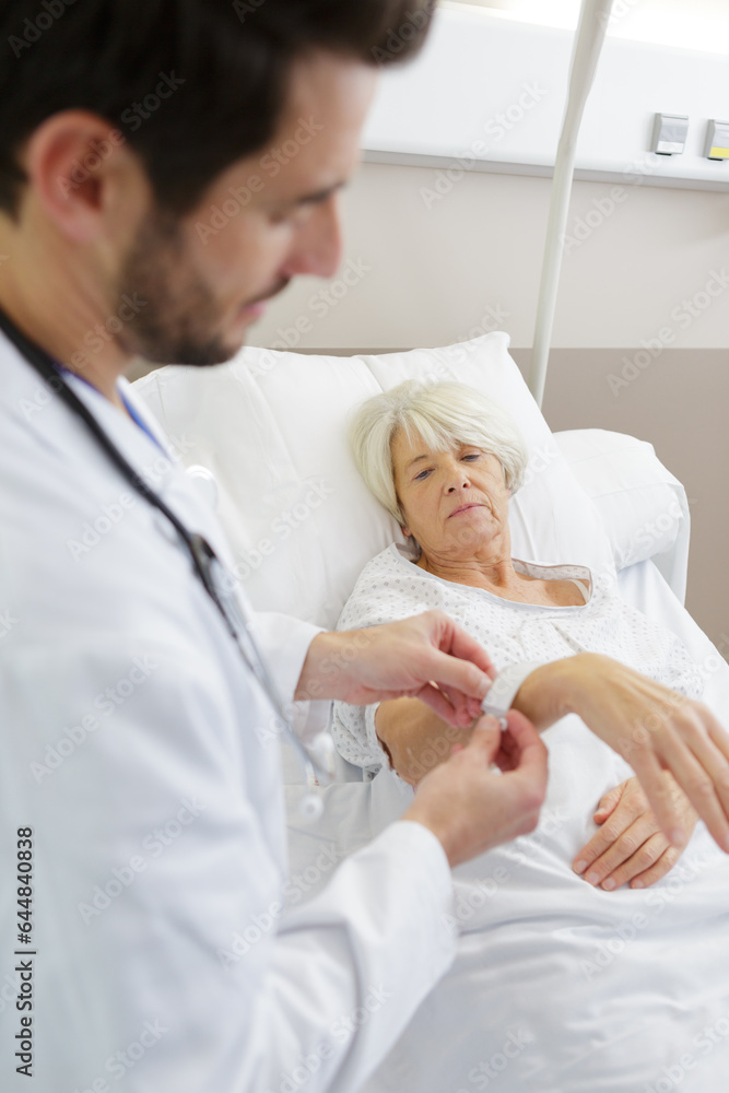 Fototapeta premium doctor securing identification tag on senior female patient in hospital