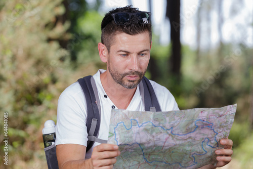 man with map on hike in countryside resting by gate