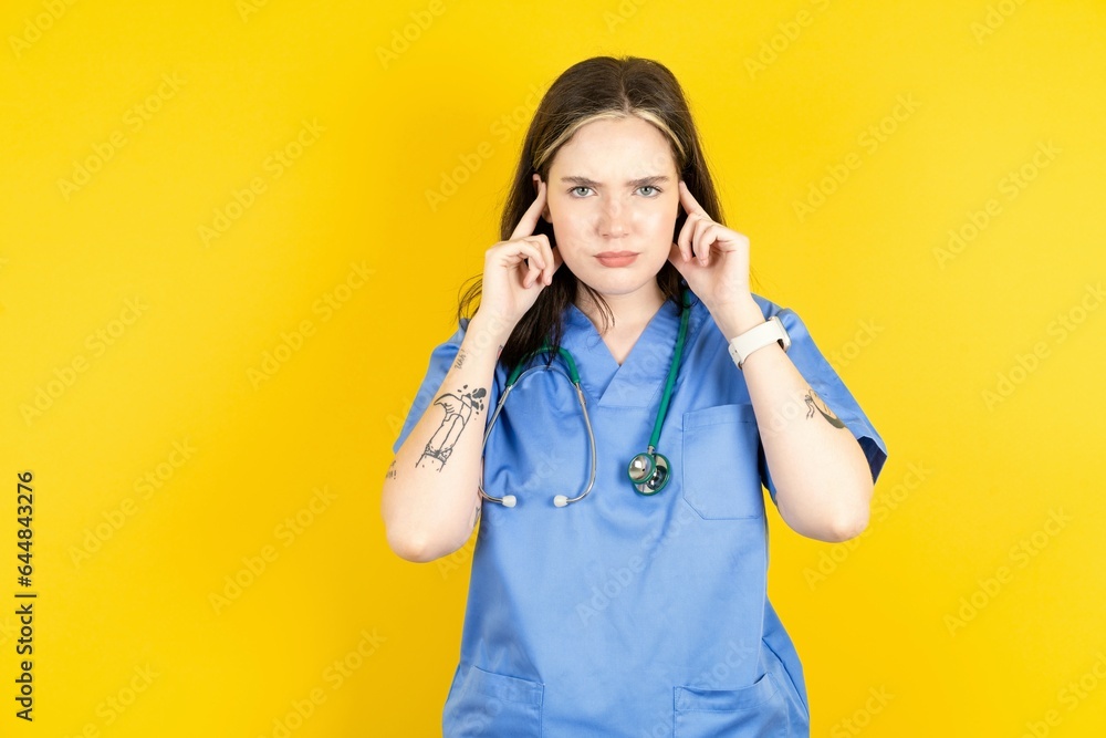 Serious concentrated Young caucasian doctor woman wearing blue medical uniform keeps fingers on temples, tries to ease tension, gather with thoughts and remember important information for exam - obrazy, fototapety, plakaty 