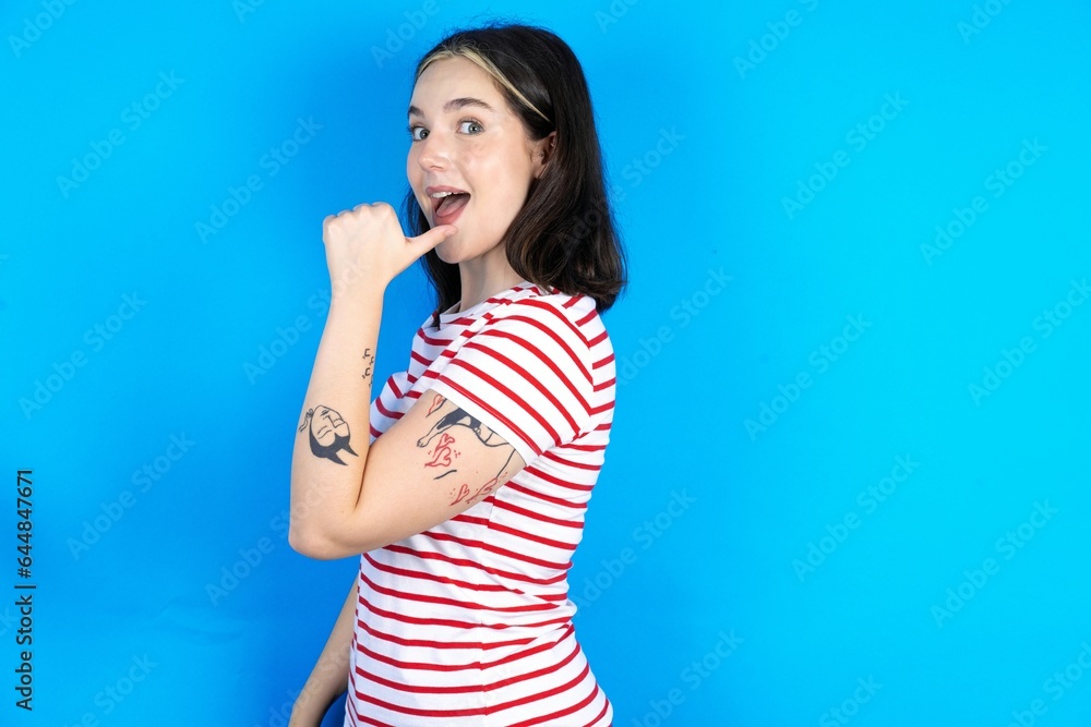 Impressed beautiful young woman wearing striped T-shirt point back empty space Impressed beautiful young woman wearing striped T-shirt point back empty space