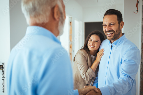 Friendly Real Estate Agent and young couple shaking hands standing in hallway, real estate agent handshaking clients at meeting, showing selling buying property for rent sale photo