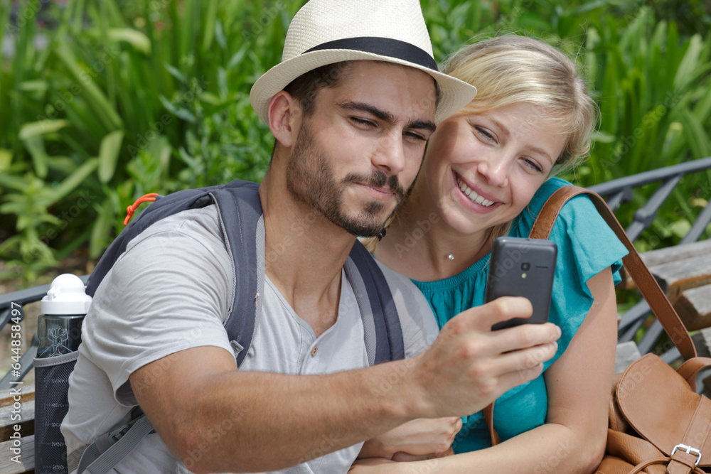 young couple on park bench taking selfie with smartphone