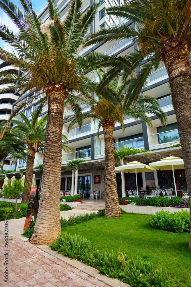 a hotel exterior in the resort town near the beach, the sidewalk and palm trees at the entrance, the background of travel during vacation