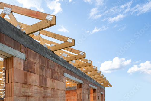 Unfinished home with red brick walls and frame roof against blue copy space sky