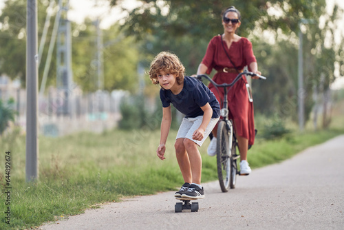 Cheerful boy on skateboard having fun with mother