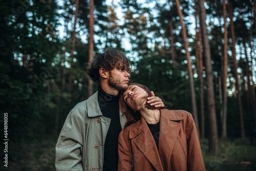 young couple in love in a fashionable coat walks through the forest. Autumn gloomy mood and a beautiful couple of models. Cinematic image © velimir