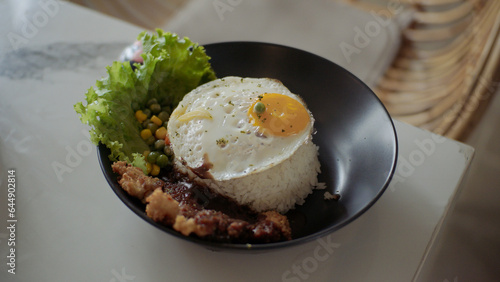 Rice bowl with sunny side up egg, chicken, vegetables and lettuce on white table in restaurant.