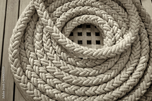 On the wooden deck of the mast yacht, a white anchor rope is folded into a round bug. photo