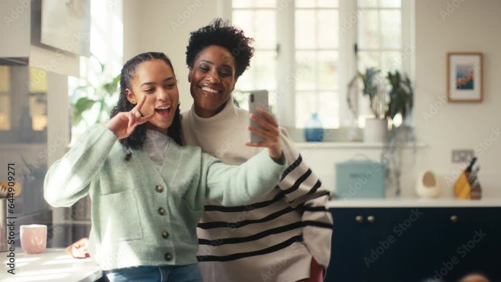Handheld shot of teenage with mature mother at home in kitchen posing for selfie to post to social media on mobile phone - shot in slow motion Handheld shot of teenage with mature mother at home in kitchen posing for selfie to post to social media on mobile phone - shot in slow motion