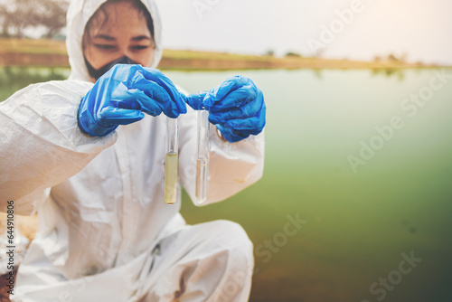 Scientist with protective suit holding a test tube with sample water in her hand. Water pollution examine concept