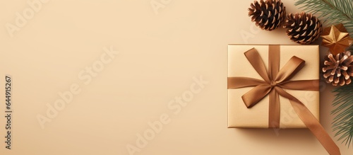 A isolated pastel background Copy space showcases a golden gift box adorned with a ribbon bow brown leaf and pine cone © HN Works