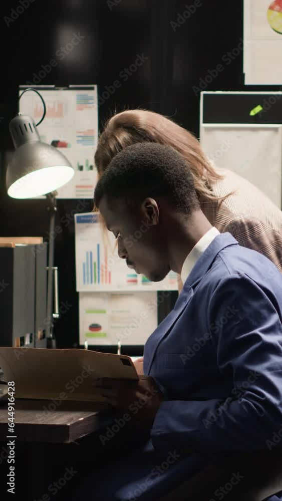 Vertical video Multiethnic investigators examine evidence, discuss the case, and gather clues in a well-organized environment. Caucasian woman carrying forensic files joins african american man in