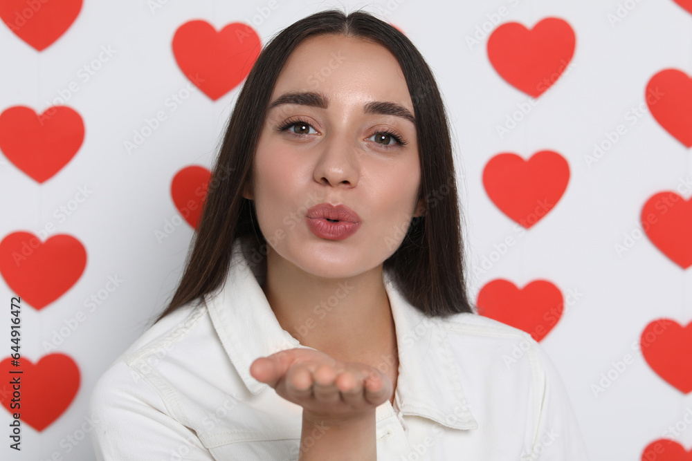 Young woman blowing kiss into camera on decorated background Young woman blowing kiss into camera on decorated background