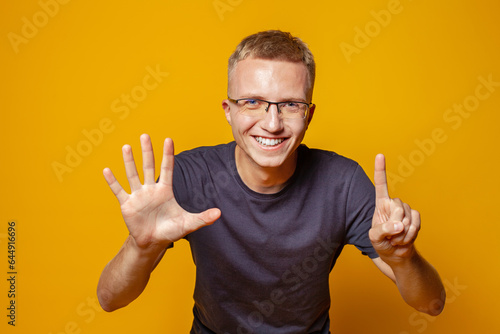Fototapet Happy man showing fingers number six on bright orange studio wall background