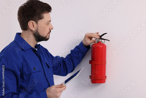 Man with tablet checking fire extinguisher indoors