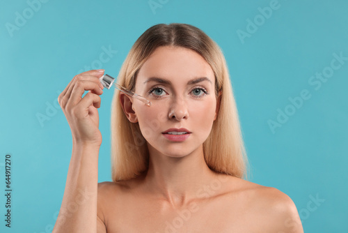 Beautiful woman applying cosmetic serum onto her face on light blue background