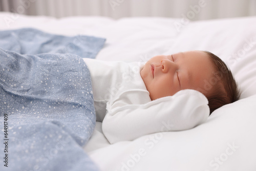 Cute newborn baby sleeping under blue blanket on bed