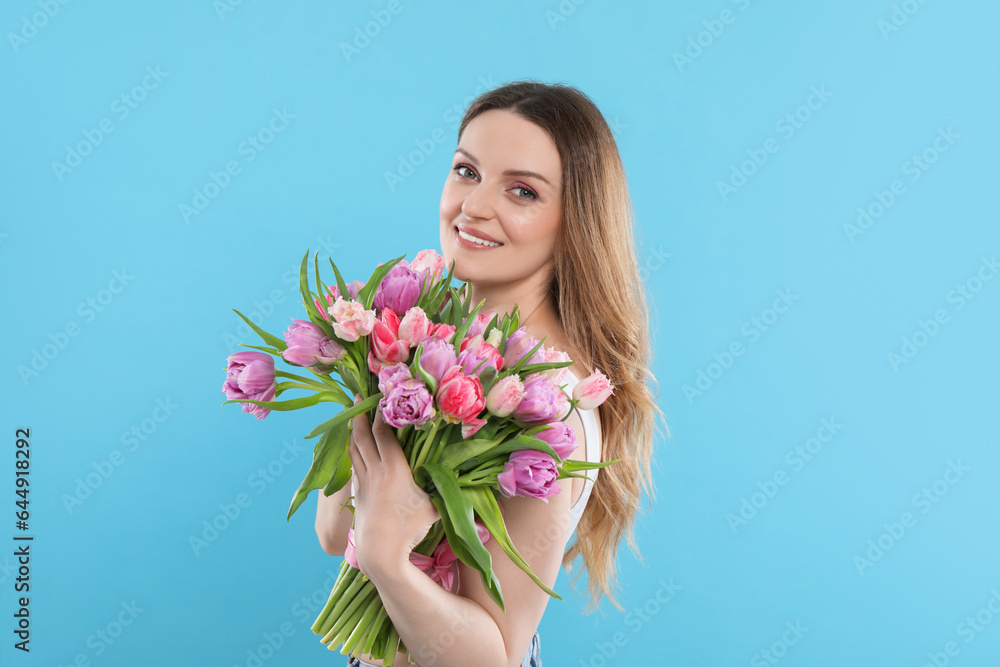 Happy young woman with bouquet of beautiful tulips on light blue background Happy young woman with bouquet of beautiful tulips on light blue background