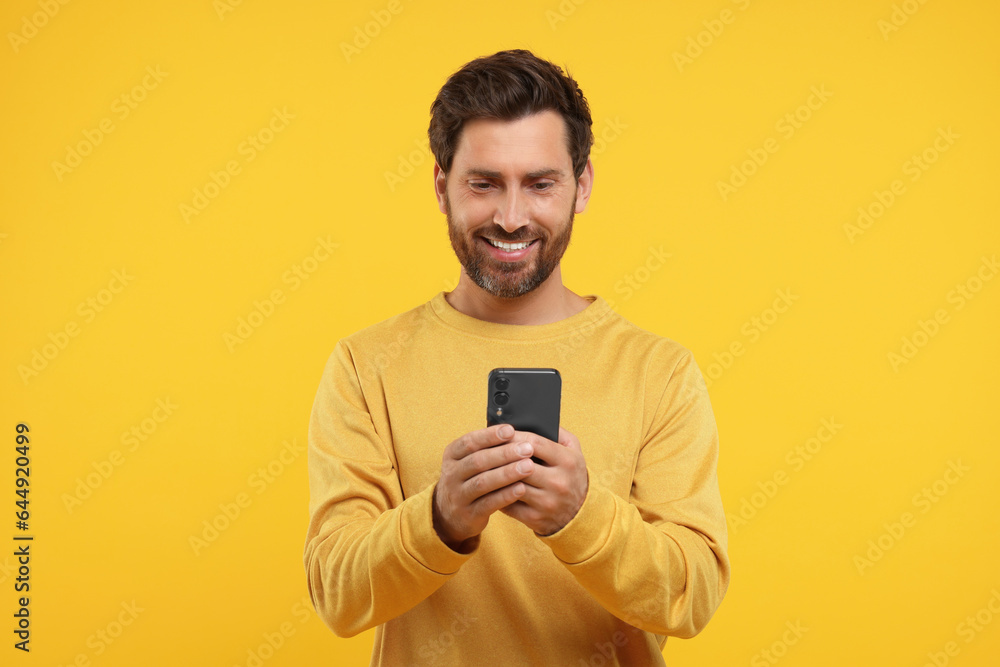 Handsome bearded using smartphone on orange background Handsome bearded using smartphone on orange background