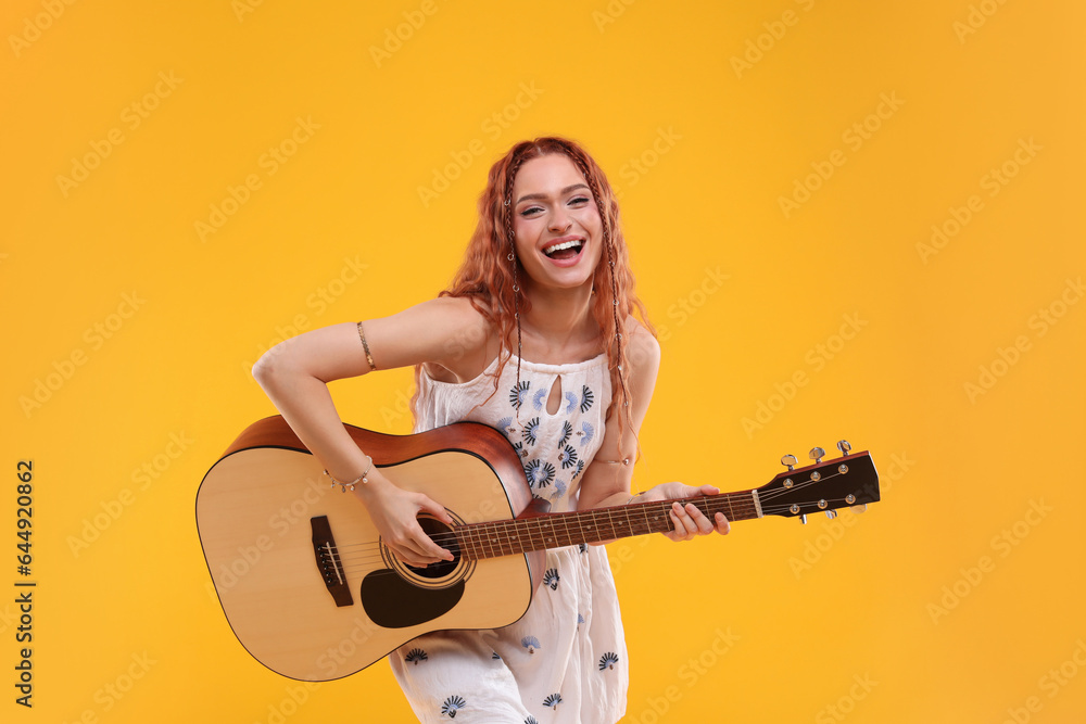 Beautiful young hippie woman playing guitar on orange background Beautiful young hippie woman playing guitar on orange background