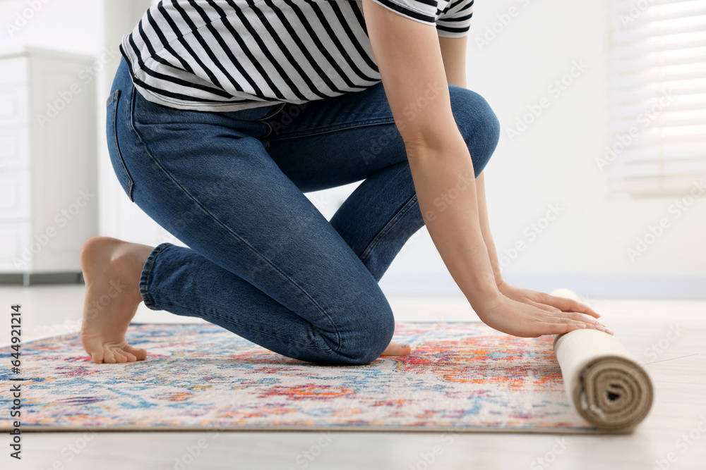 Obraz premium Woman unrolling carpet with beautiful pattern on floor in room, closeup