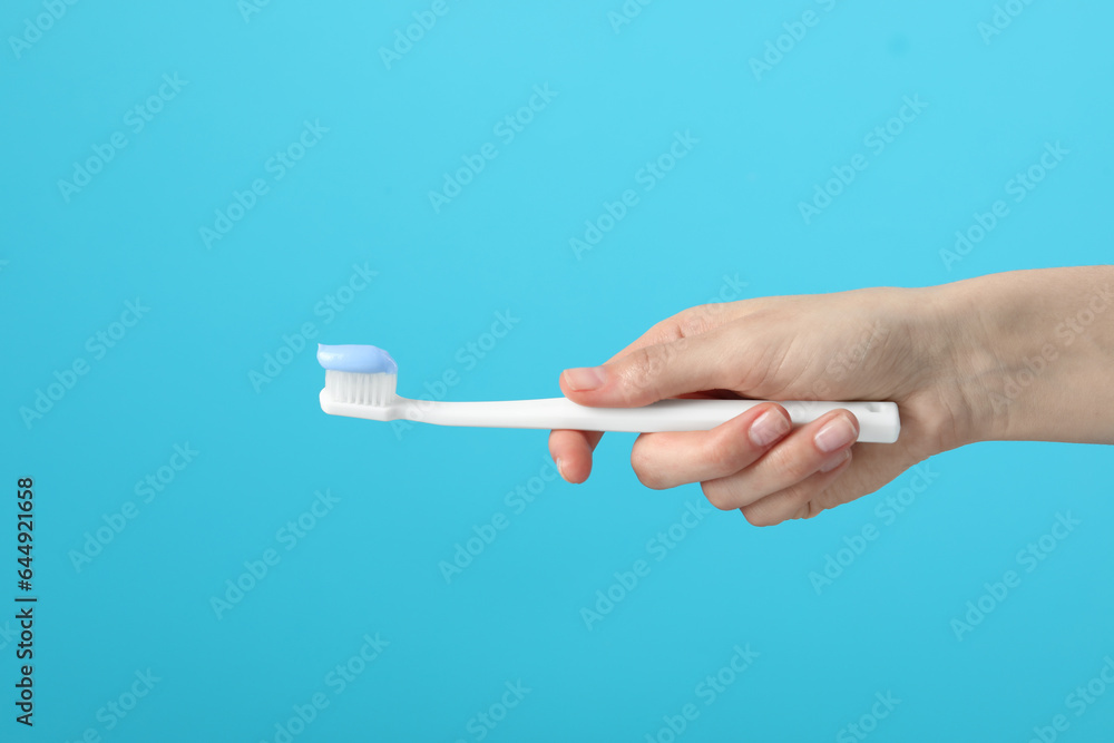 Woman holding toothbrush with paste on light blue background, closeup Woman holding toothbrush with paste on light blue background, closeup