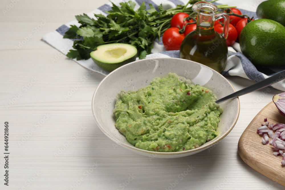 Preparing delicious guacamole in bowl and ingredients on white wooden table