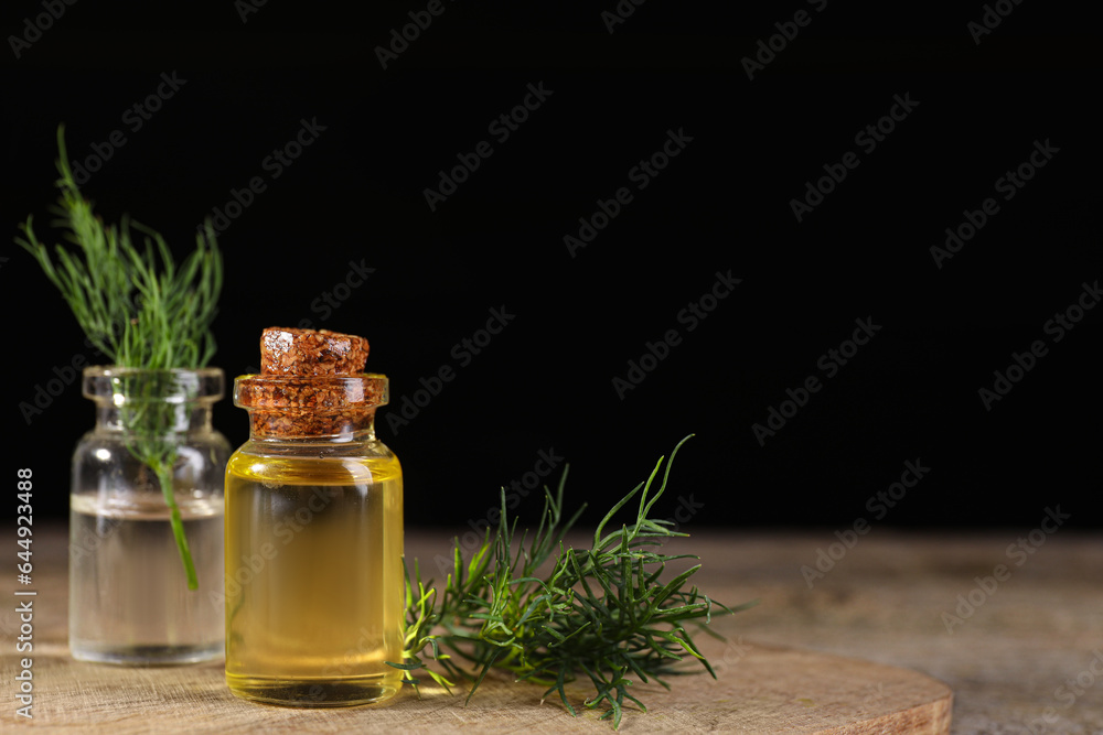 Bottles of essential oil and fresh dill on wooden table against black background. Space for text Bottles of essential oil and fresh dill on wooden table against black background. Space for text