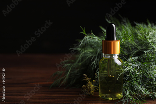 Bottle of essential oil and fresh dill on wooden table against dark background, closeup. Space for text