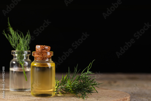 Bottles of essential oil and fresh dill on wooden table against black background. Space for text