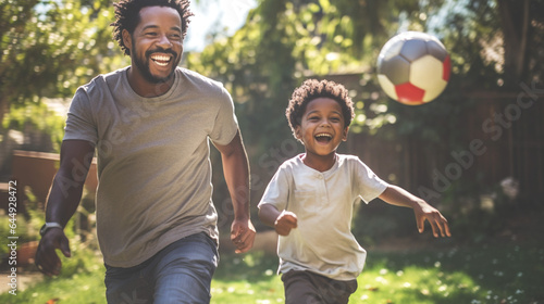 Middle-aged father, dark-skinned, smiling, playing soccer in the backyard with his son. The game showcases strong bonds and valuable life lessons being passed on. Modern fatherhood. Banner. © Nataliia