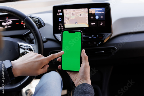 The green screen of the phone is chroma key in the car. Driver is sitting in the car and watching her smartphone with green screen at day. Man holding mobile phone on the background of a car interior photo