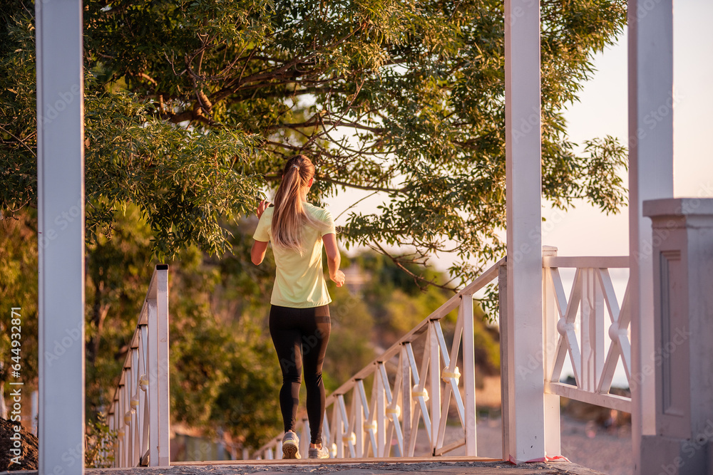 Young woman in sportswear is exercising, jogging on wooden stairs in the rays of the dawn sun. Going in for sports on street of the city. Girl posing in the concept of sport, fitness. Morning routine