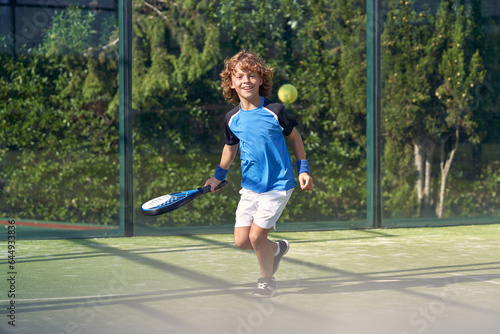 Happy boy playing padel on court at daytime