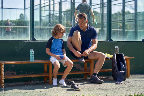 Man with son putting on sports wear against windows of padel cou