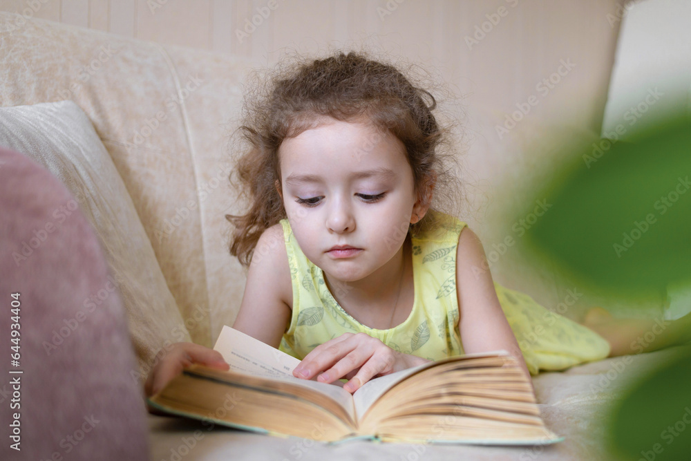 smart little girl reading book at home on couch. child learning read. children's education. smart little girl reading book at home on couch. child learning read. children's education.