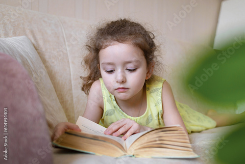 smart little girl reading book at home on couch. child learning read. children's education. © Елена Якимова