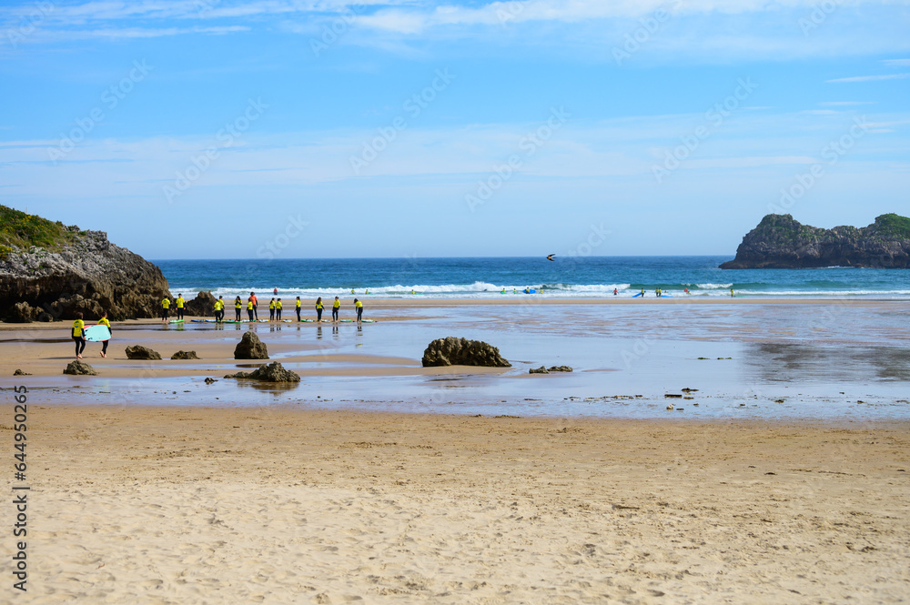 Young surfers train on Playa de Palombina Las Camaras in Celorio, Green coast of Asturias, North Spain with sandy beaches, cliffs, hidden caves, green fields and mountains