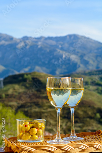 Glasses of dry white wine and spanish tapas olives in bowl with mountains peaks on background in sunny day