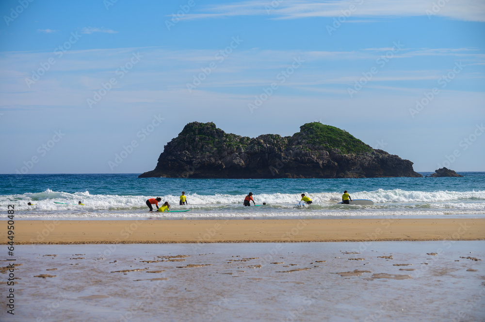 Obraz premium Young surfers train on Playa de Palombina Las Camaras in Celorio, Green coast of Asturias, North Spain with sandy beaches, cliffs, hidden caves, green fields and mountains