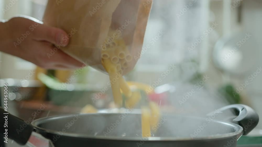 Hands of man putting rigatoni from paper bag into cooking pot with boiling water, preparing Italian pasta in the kitchen. Close-up impersonal shot Hands of man putting rigatoni from paper bag into cooking pot with boiling water, preparing Italian pasta in the kitchen. Close-up impersonal shot