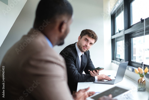 Caucasian businessman talking with black colleague on workspace in modern office.
