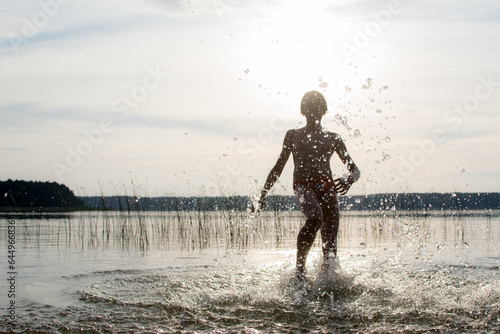 A slender guy child teenager runs along the water along the coast at sunset  splashing from the water.