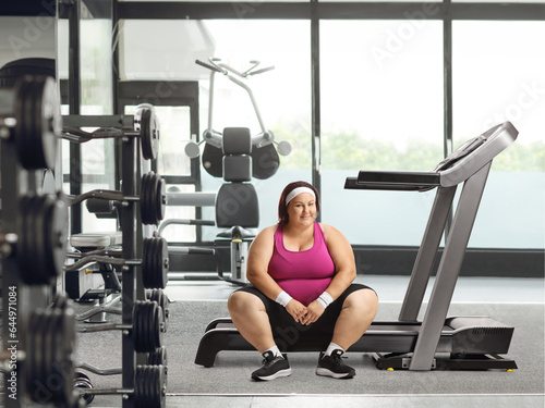 Smiling overweight woman resting on a treadmill at a gym